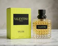 Valentino Acqua di Roma Eau de Toilette bottle with a black cap next to its lime green and black packaging box, set on a marble surface with a neutral background.